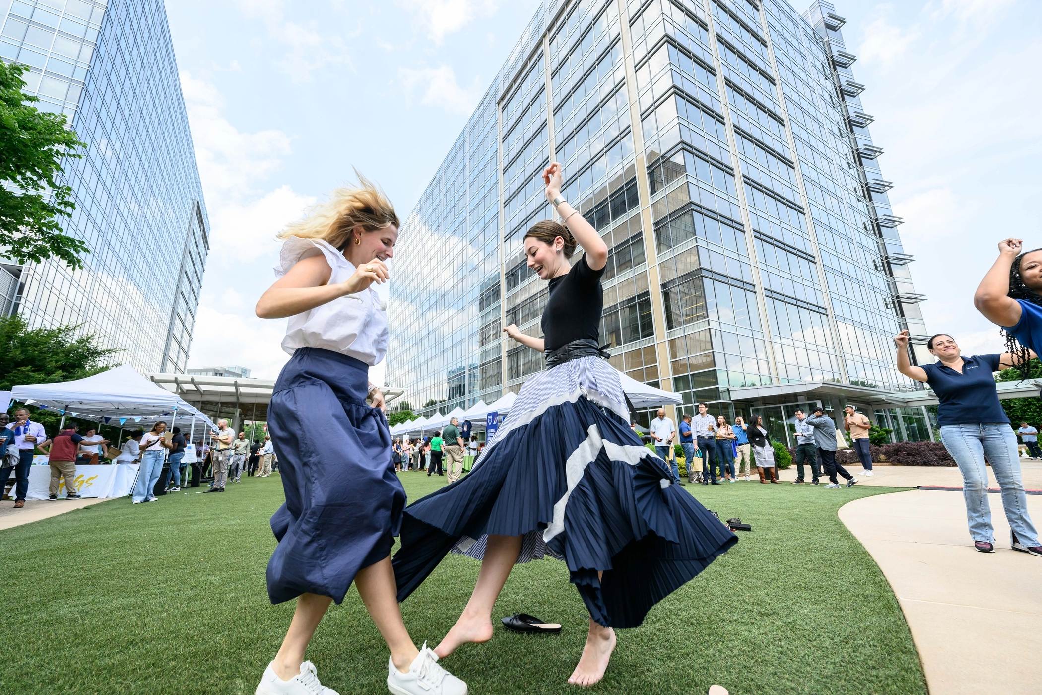 Cox employees dancing in a grassy area with a large building in the background