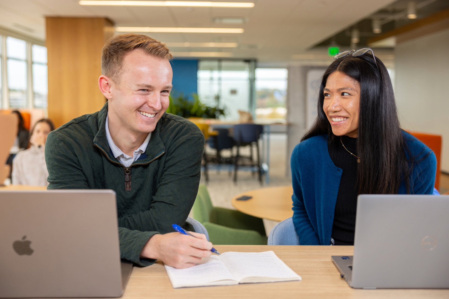 a person and person sitting at a table with laptops and a book