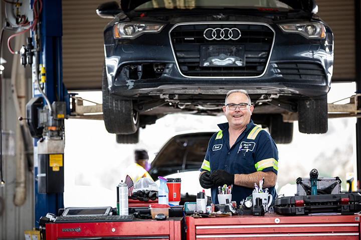 a Cox auto tech working on a car and smiling at the camera
