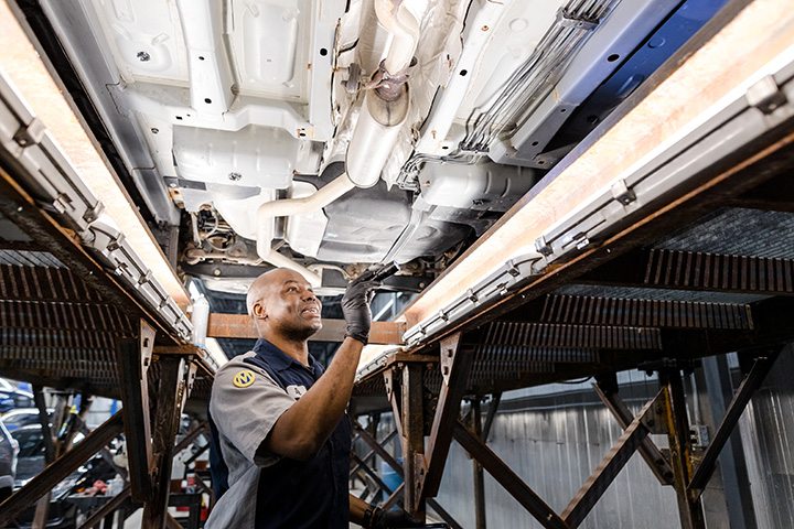 a Cox auto tech inspecting the bottom of a car with a flashlight