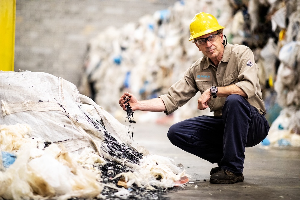 Nexus Circular employee wearing a hard hat and holding a pile of recycled plastics