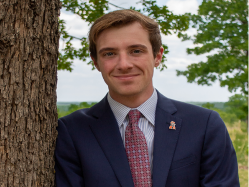 a person in a suit leaning against a tree